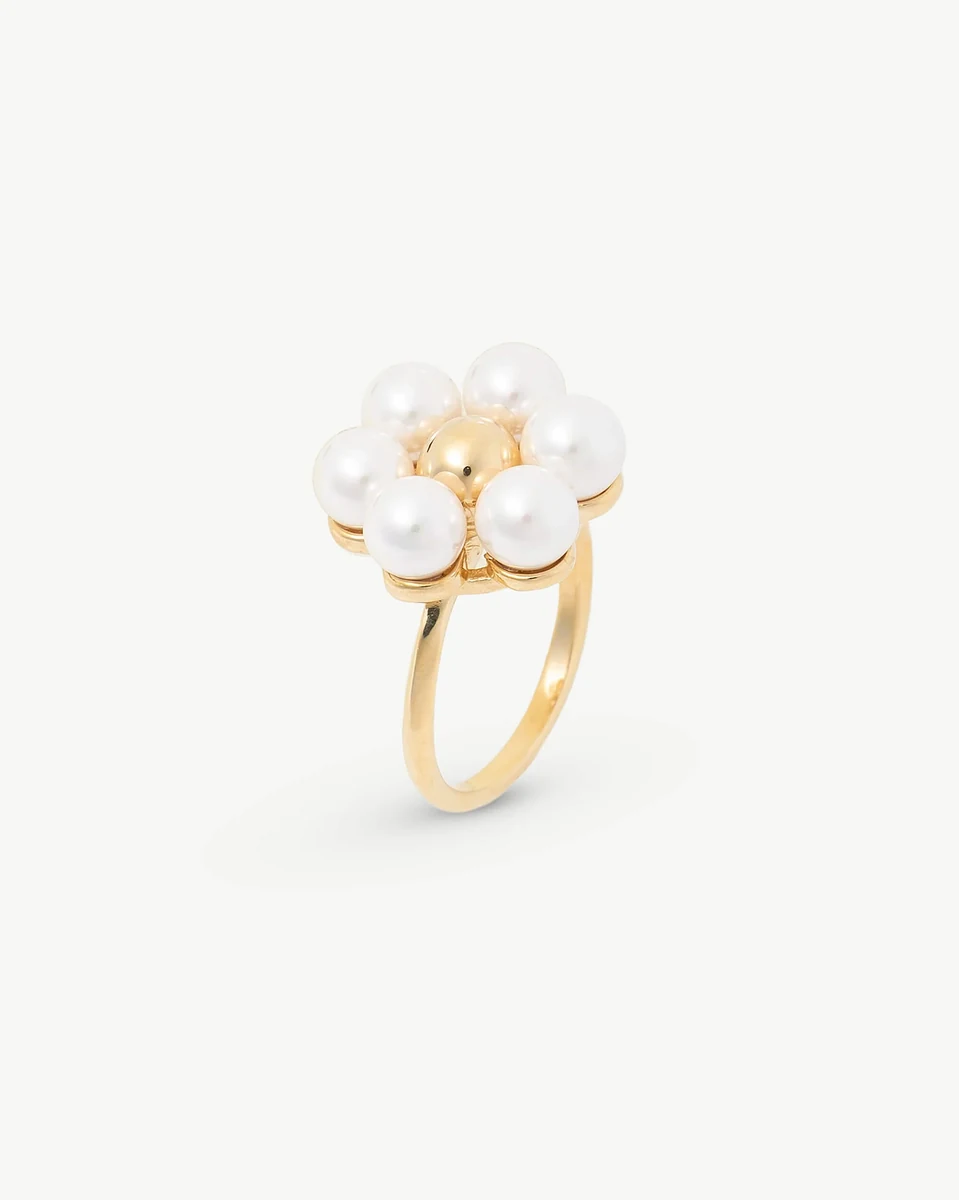 Anillo de diseño floral con perlas blancas, vista lateral en ángulo, sobre fondo blanco.