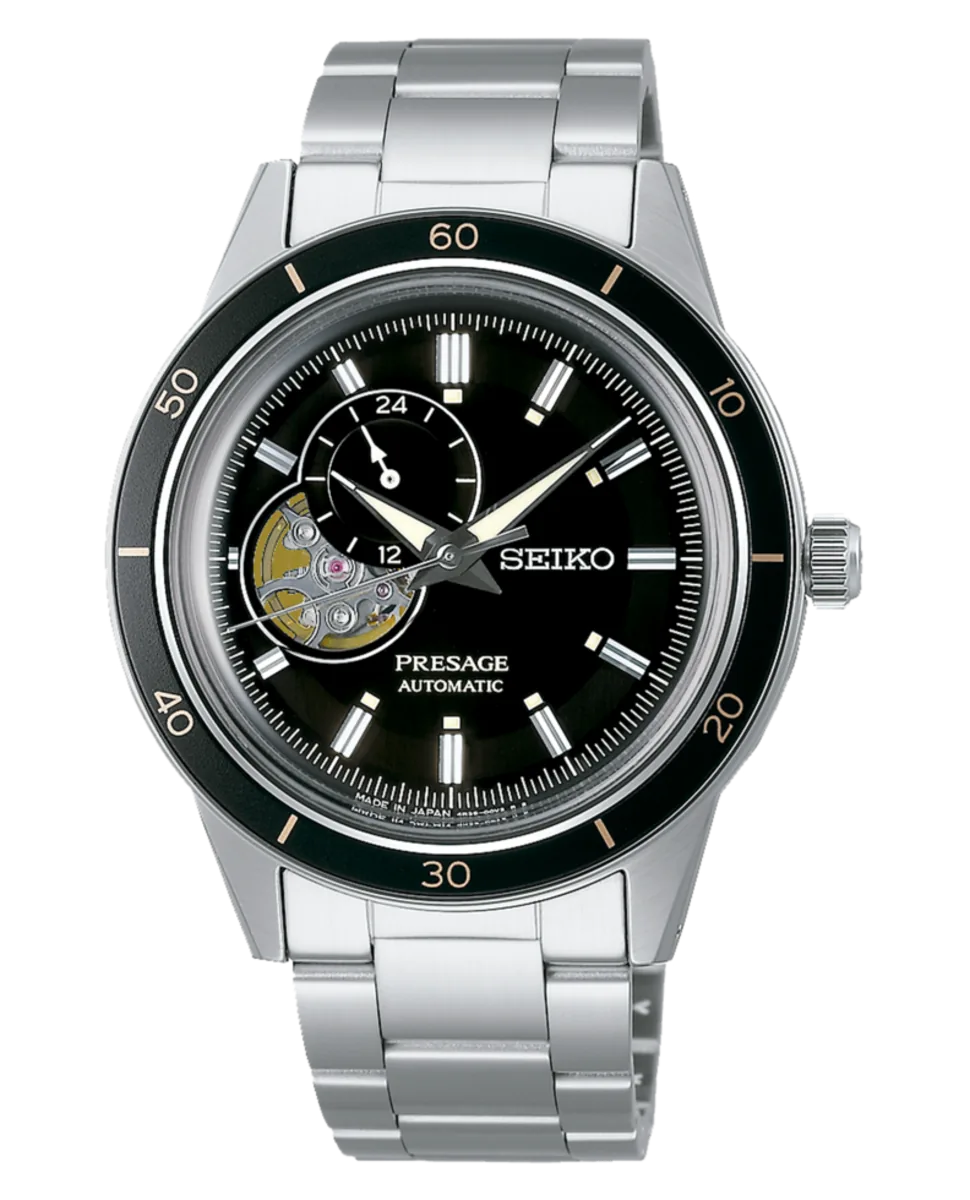 Vista frontal completa del reloj, esfera negra con maquinaria vista y brazalete de acero, fondo blanco.