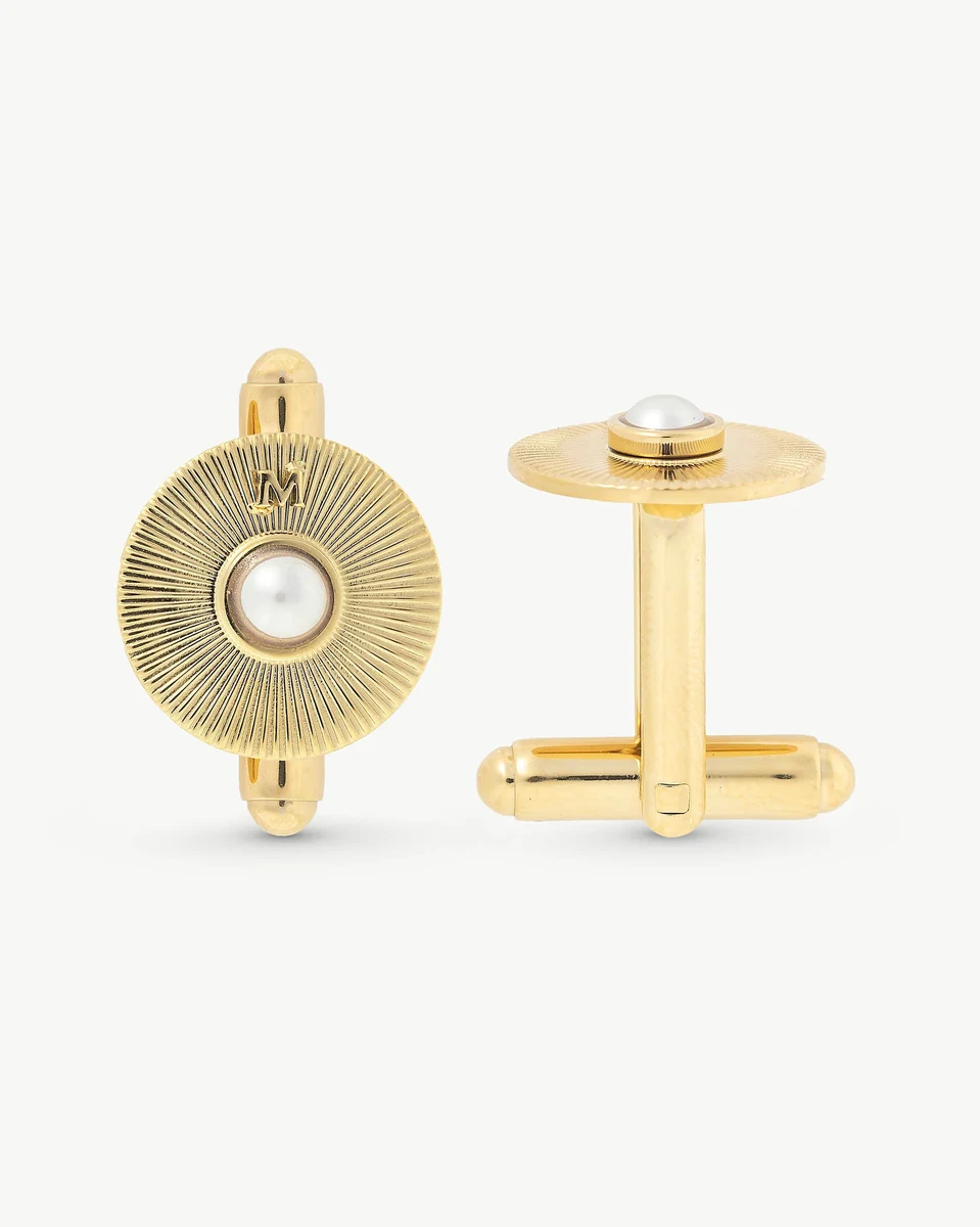 Vista frontal y lateral de los gemelos sobre fondo blanco, resaltando el acabado dorado y la perla central.