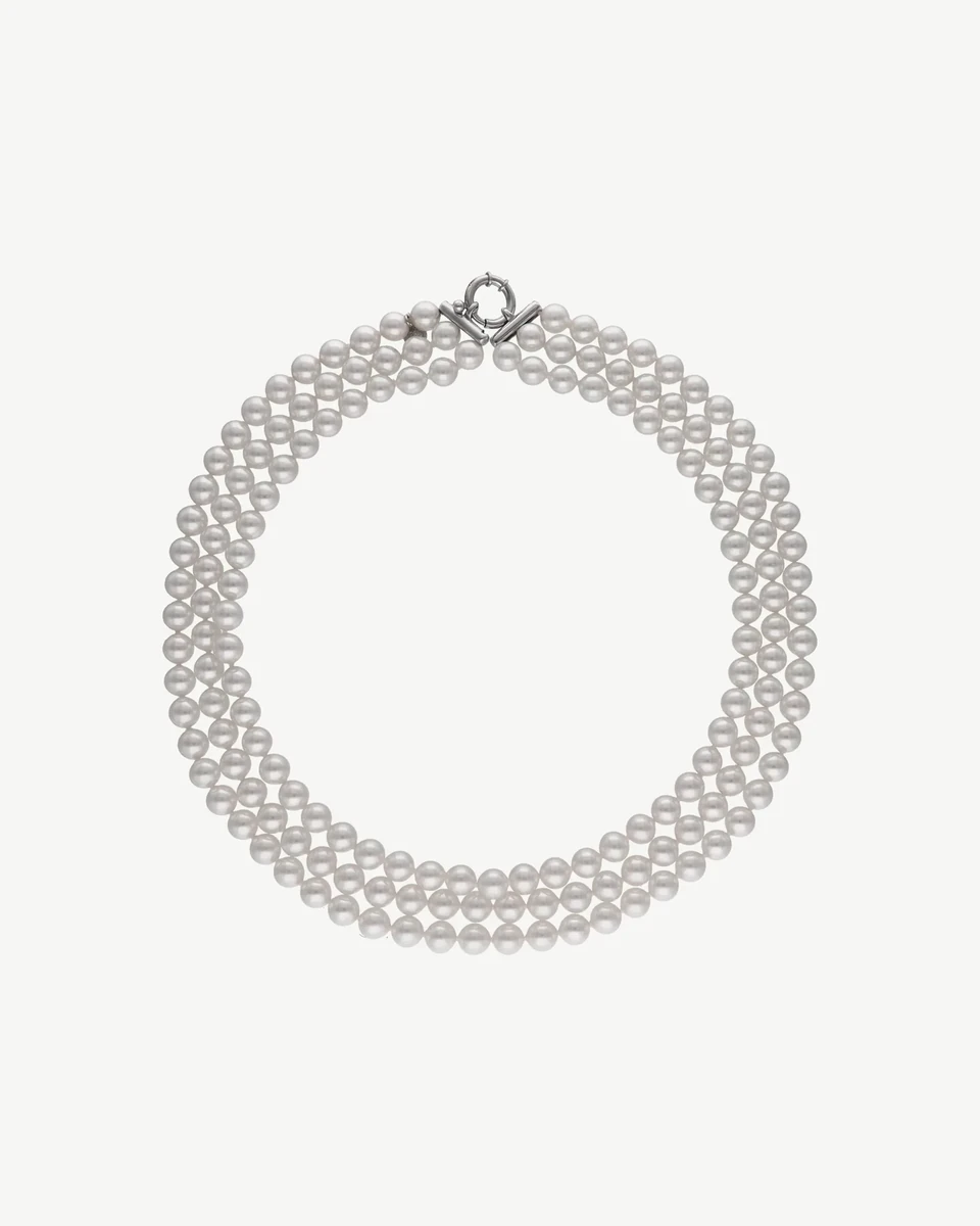 Collar de tres vueltas de perlas blancas dispuesto en círculo sobre fondo blanco, vista cenital.
