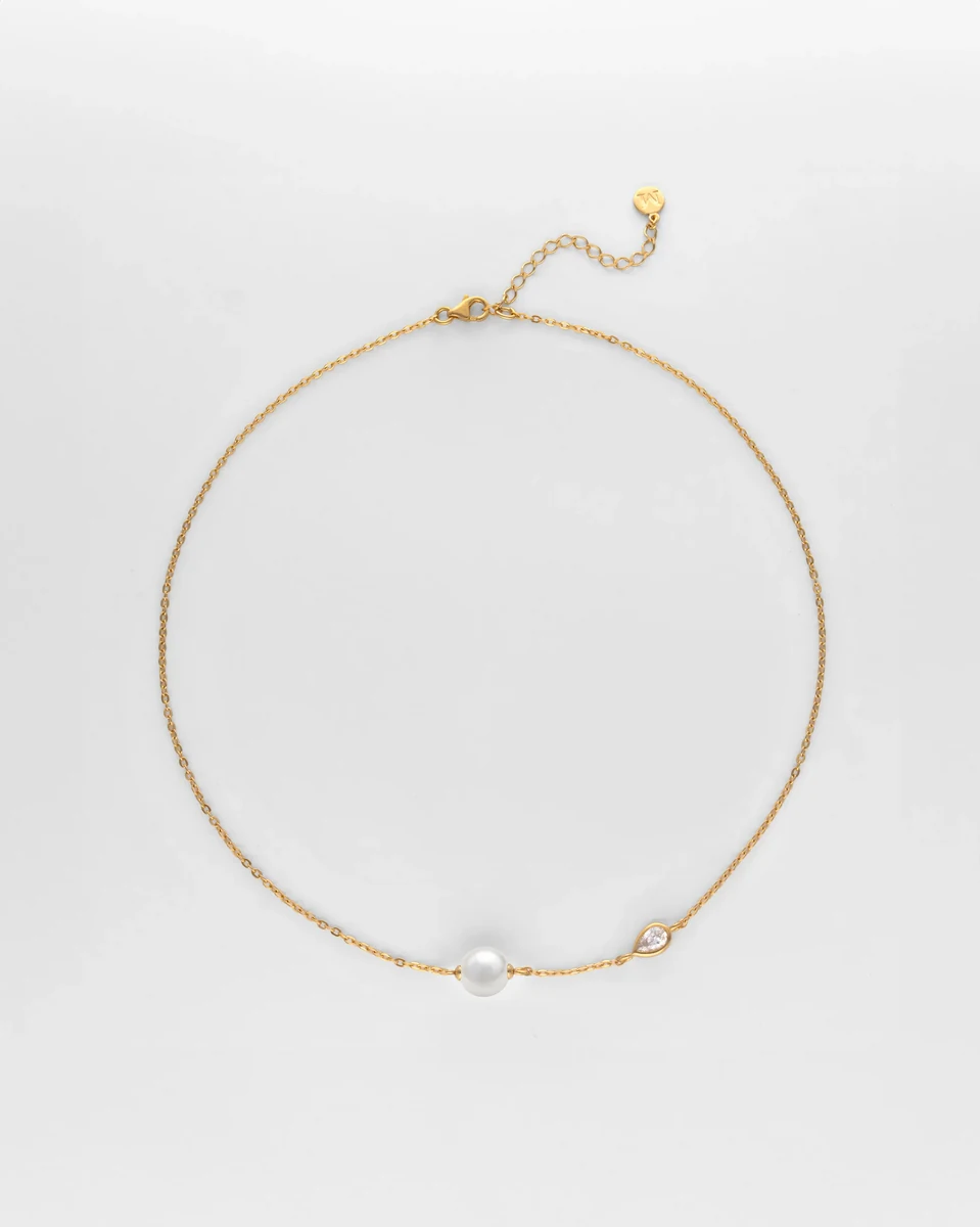 Feine Halskette kreisförmig auf weißem Hintergrund arrangiert, mit Perle und Zirkoniastein.