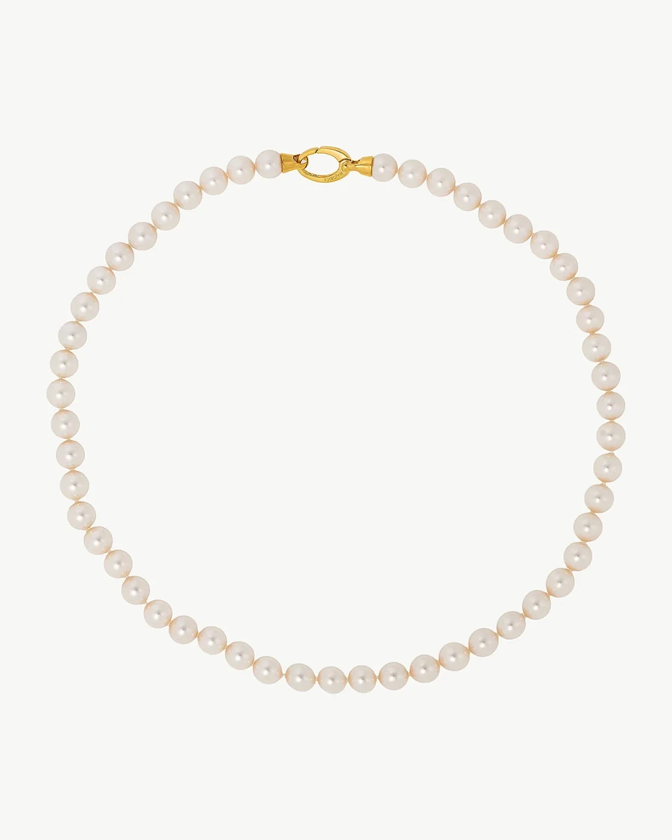 Collar de perlas dispuesto en círculo sobre fondo blanco, vista cenital con detalle del cierre dorado.